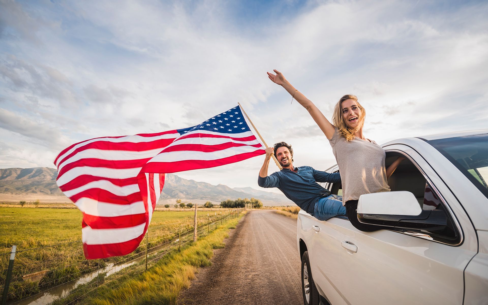 A man and a woman are sitting in a car holding an american flag.