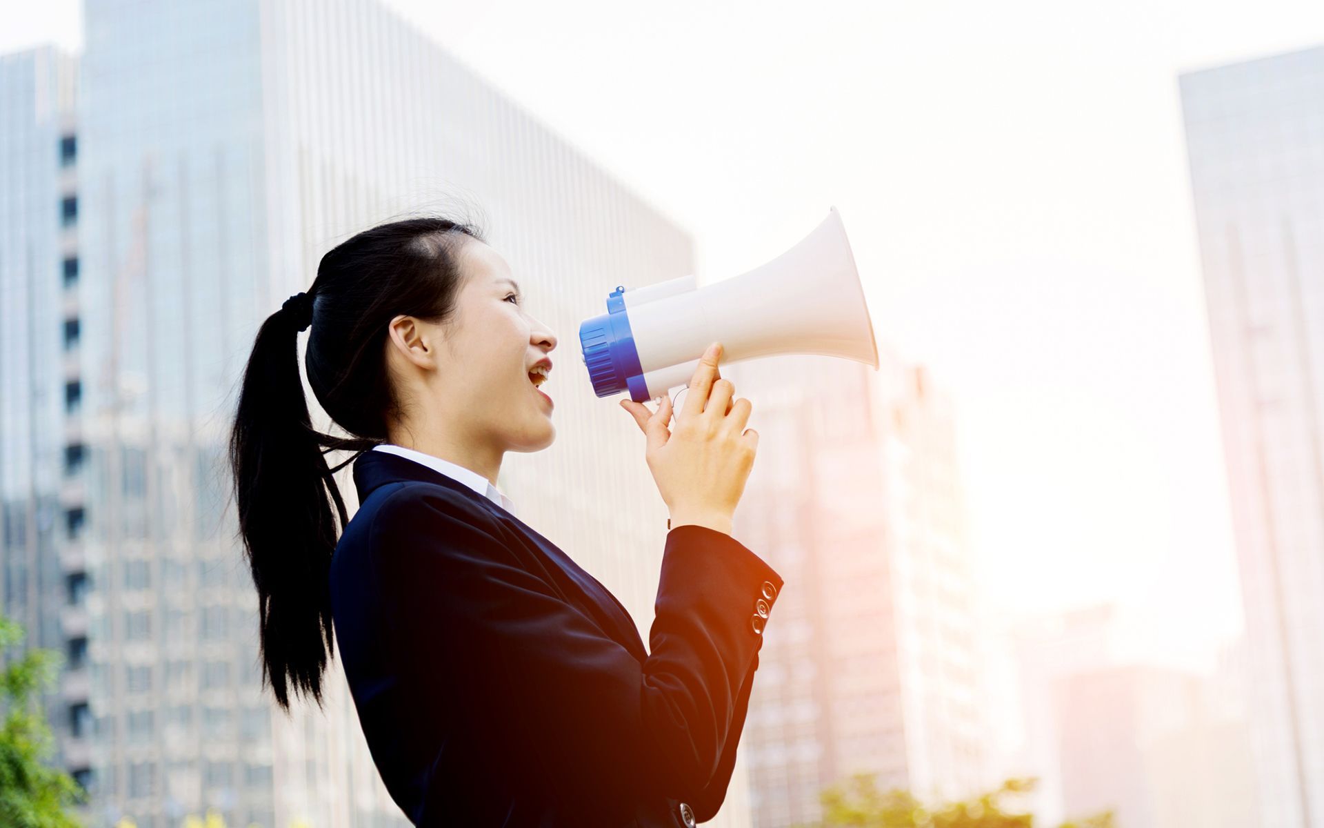 A woman in a suit is holding a megaphone in front of a building.