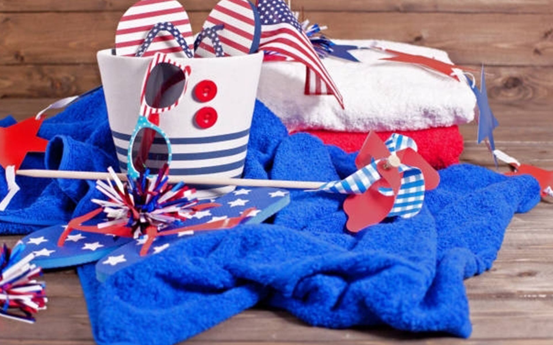 A wooden table topped with blue towels , flip flops , sunglasses and a bag.