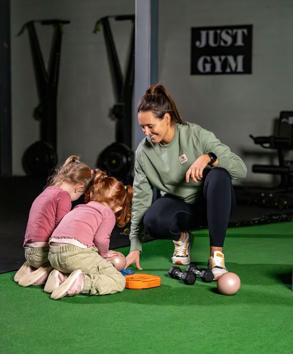 A woman is squatting down with two little girls in a gym.