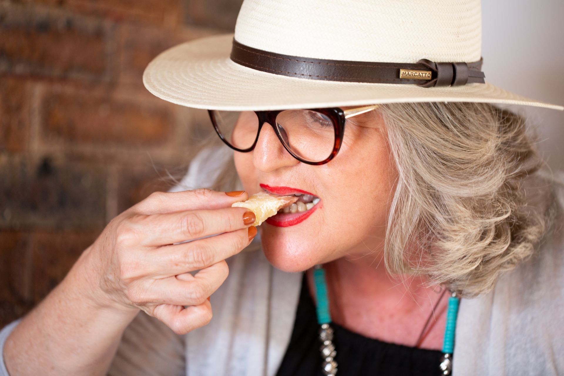 Uma mulher usando chapéu e óculos está comendo um pedaço de comida.