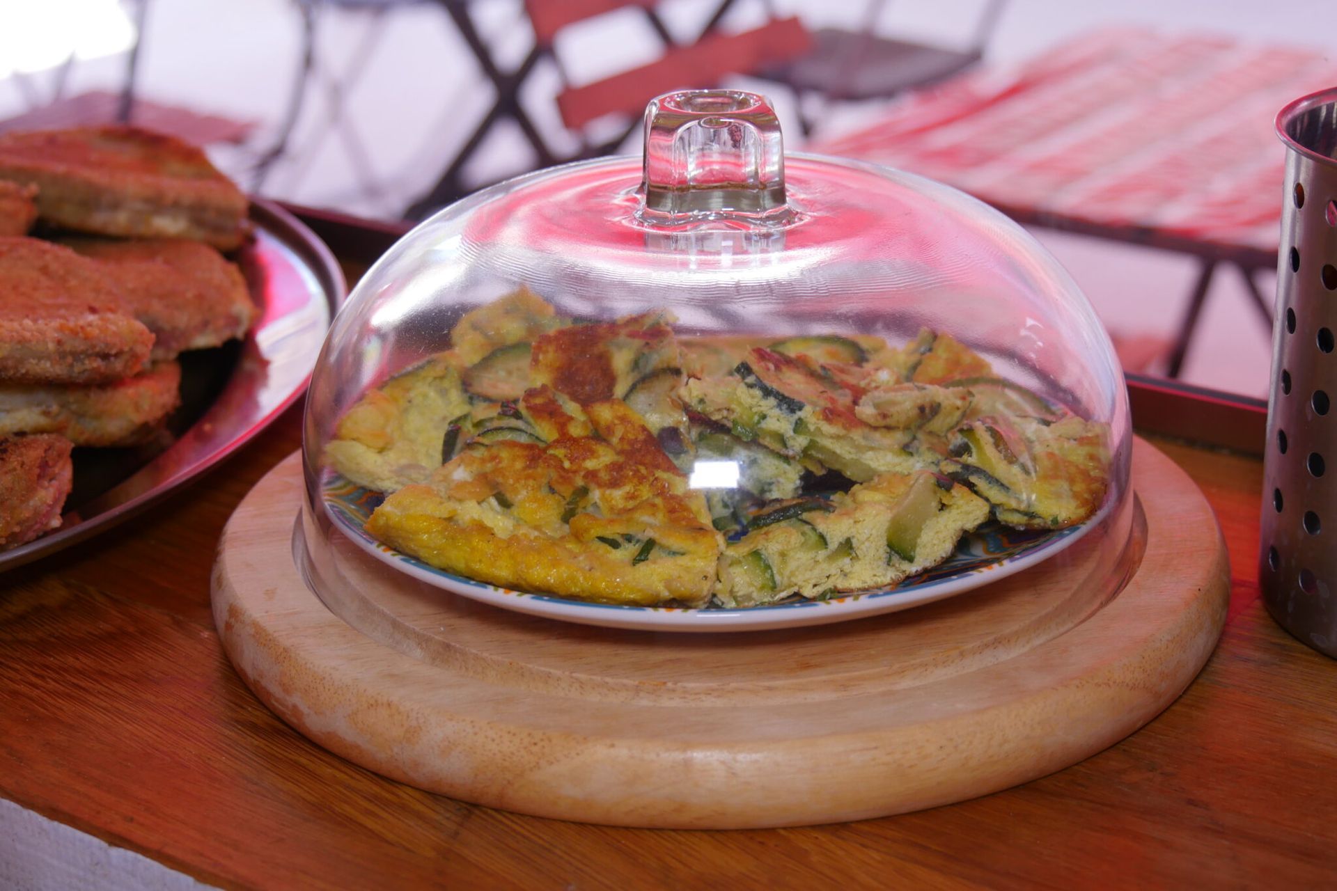 una frittata di zucchine su un vassoio di legno sotto una campana di vetro .