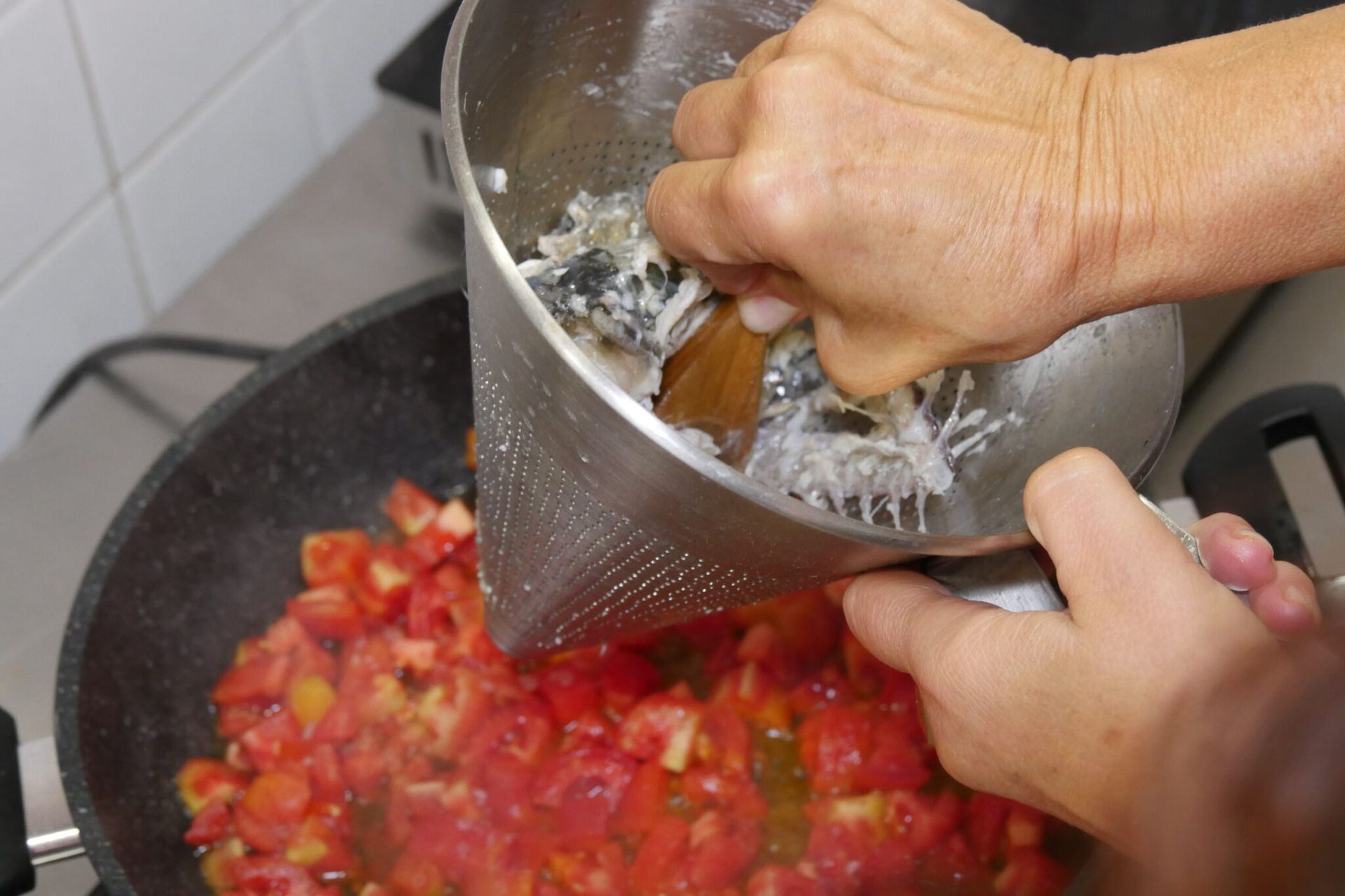 una persona sta versando cibo in una padella con un cucchiaio di legno .