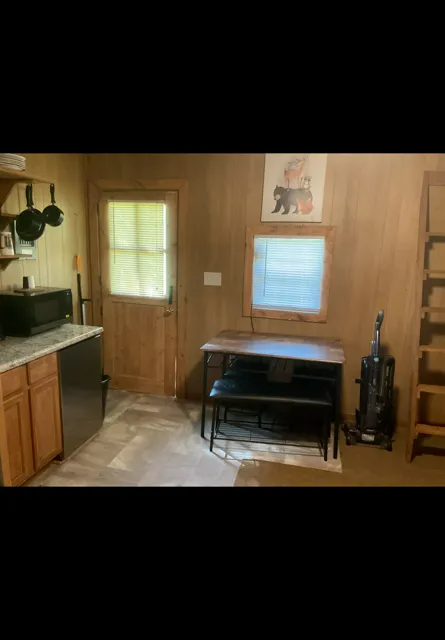 Wood-paneled room with a desk under a window, a door, and a computer desk on the left.
