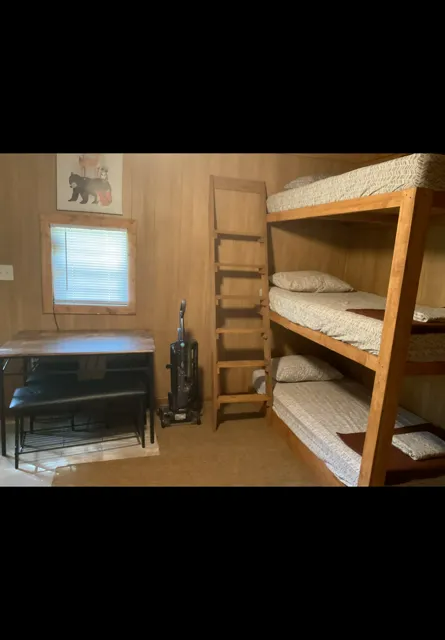 Small room with bunk beds, a desk by the window, and a ladder against wood-paneled walls.