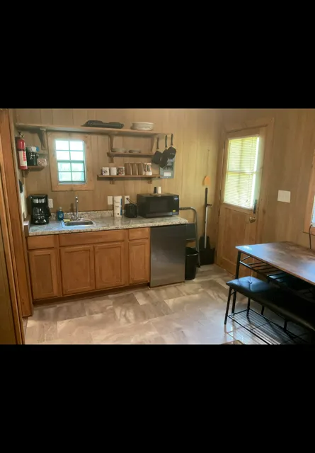 Small kitchen with wooden cabinets, stove, sink, fridge, and a table by the window.