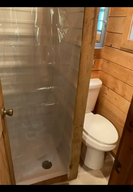 Small rustic bathroom with a shower stall and white toilet next to a wood-paneled wall.