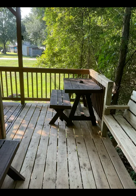 Wooden porch with picnic table, bench, and trees overlooking a grassy yard