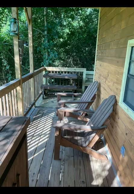 Wooden porch with two Adirondack chairs, railing, and a bench overlooking trees and a forested yard