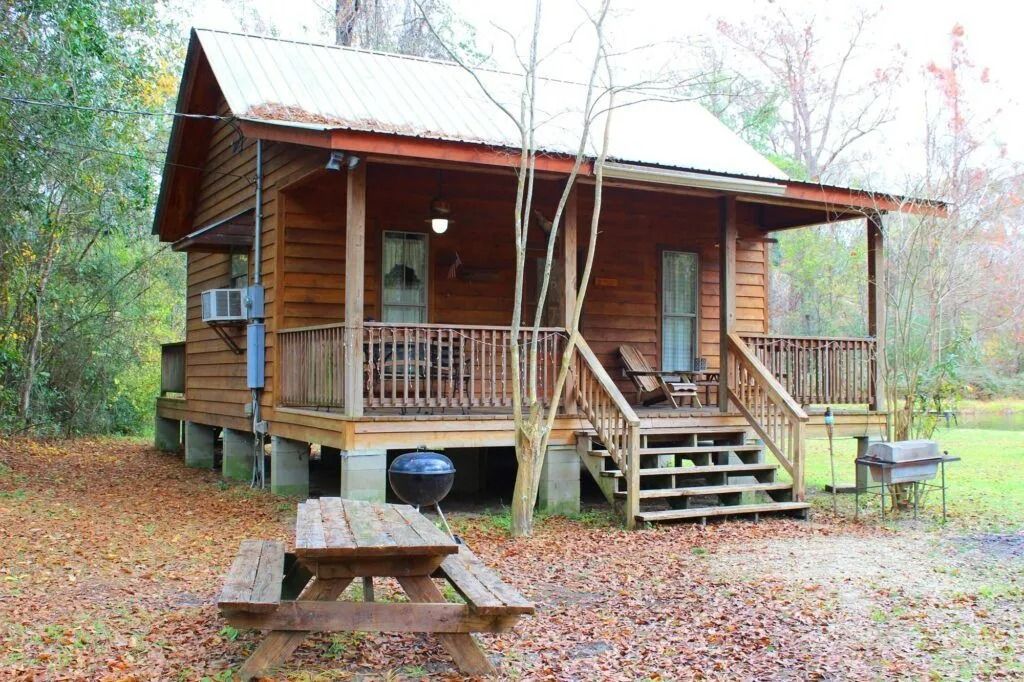 Rustic wooden cabin with porch, steps, and picnic table in a leaf-covered wooded setting