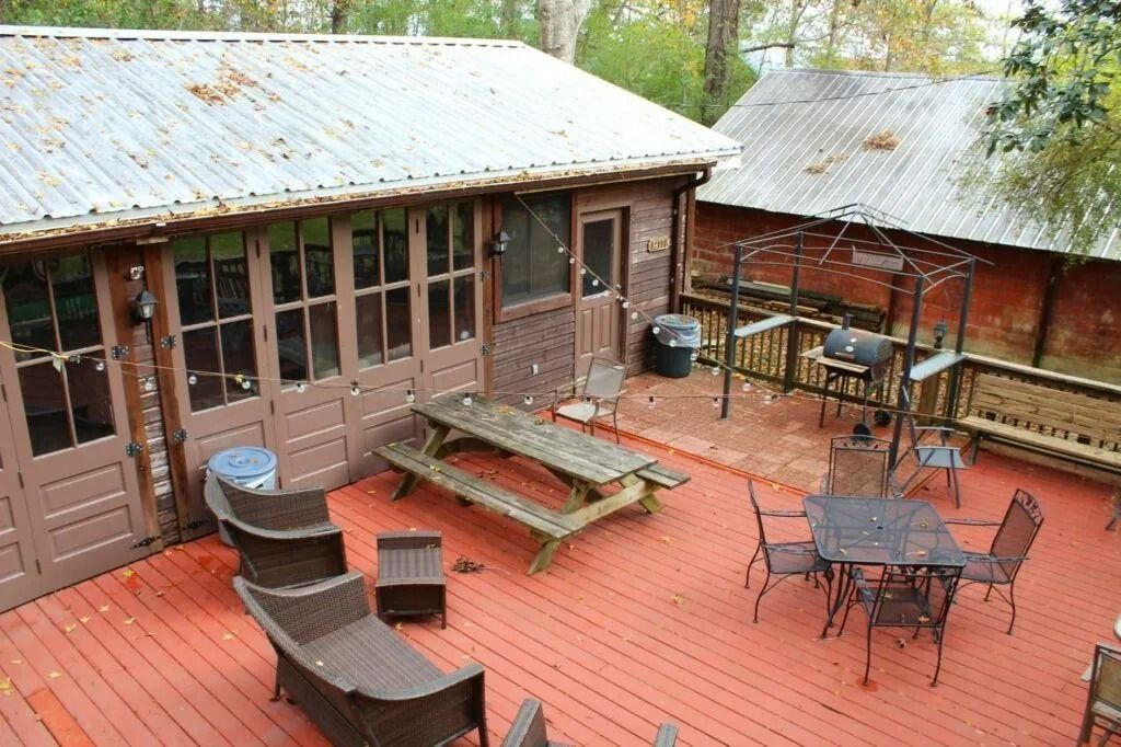 Wooden deck patio with picnic table, chairs, and grill beside a rustic cabin, viewed from above