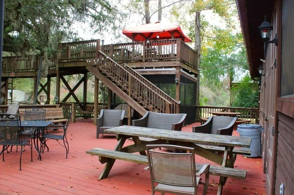 Outdoor wooden deck with stairs, patio furniture, and red umbrella under trees