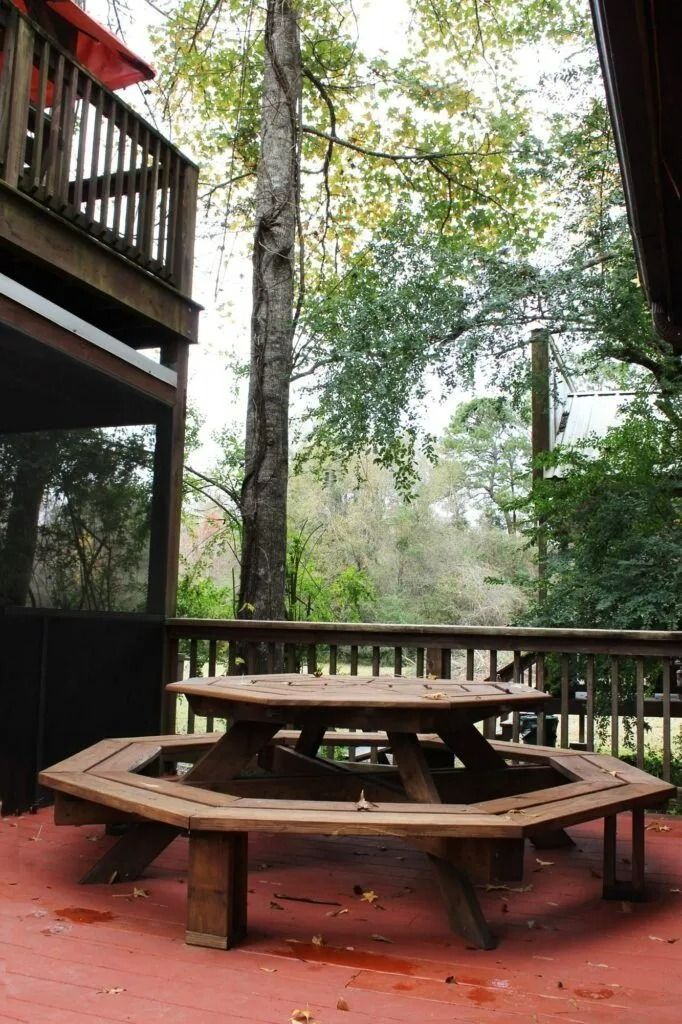 Wooden picnic table on a red deck surrounded by tall trees in a forest setting