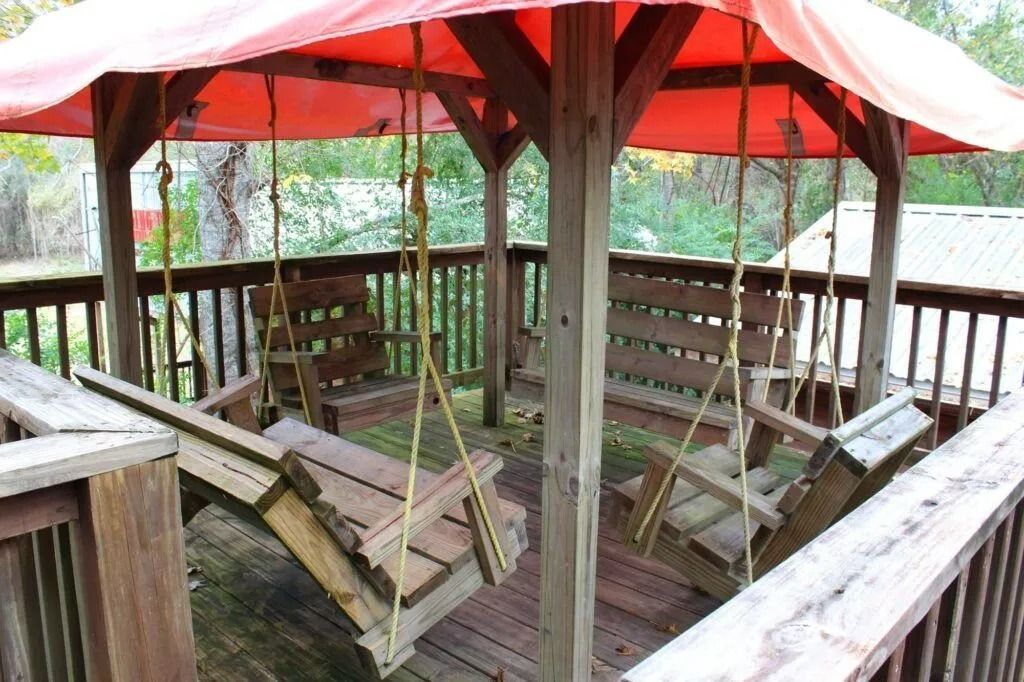Rustic wooden gazebo with red-and-white canopy and benches in a fenced outdoor area