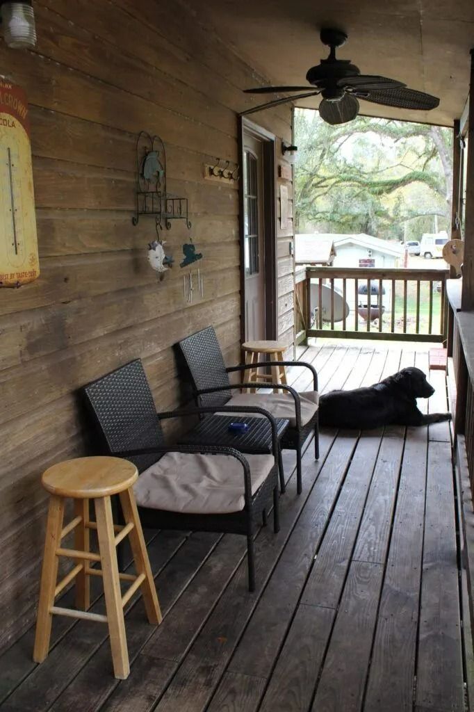 Covered wooden porch with chairs, stool, ceiling fan, and a black dog lying on the floor.