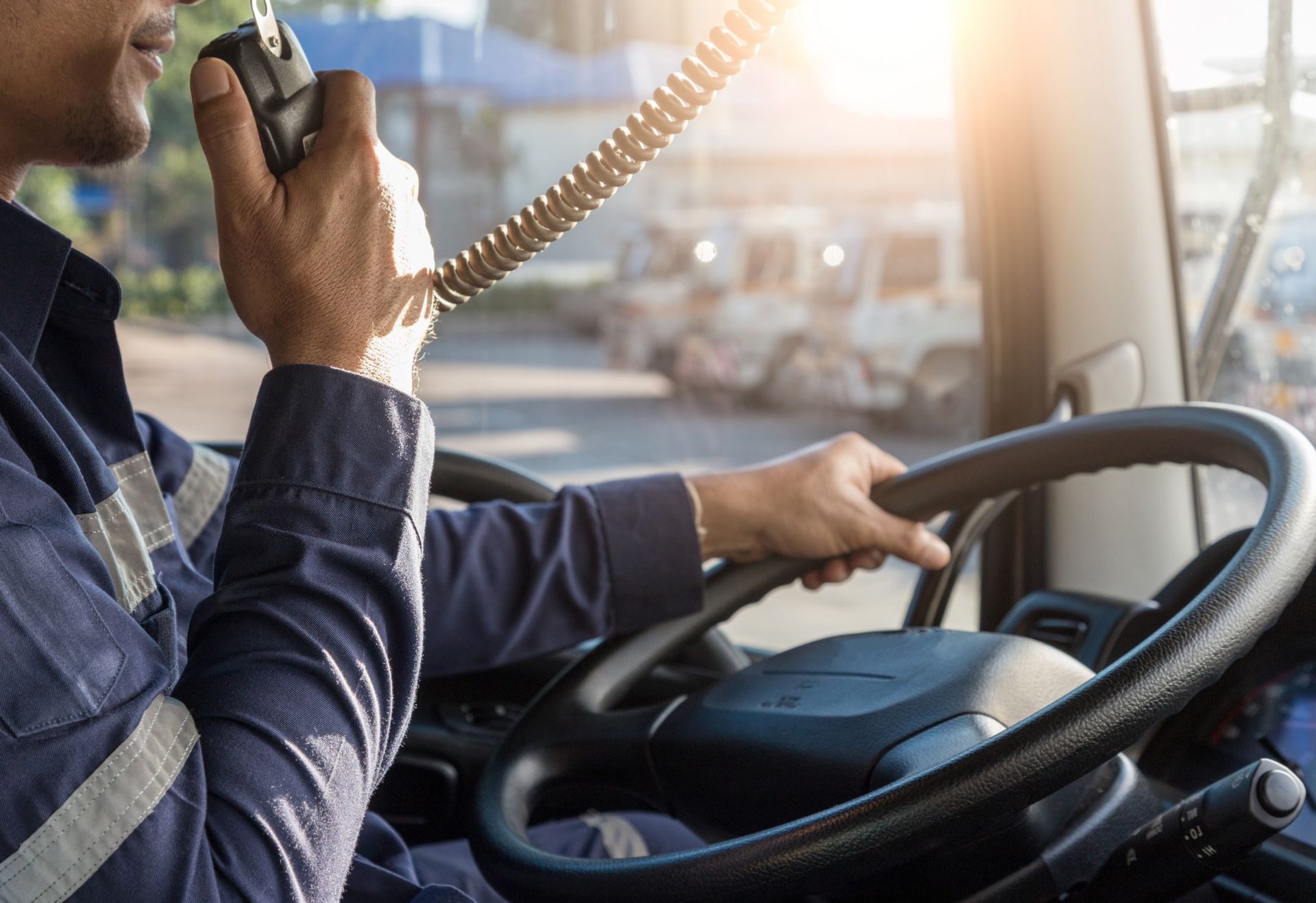 Driver holding a radio and steering wheel in a vehicle; bright sunlight.