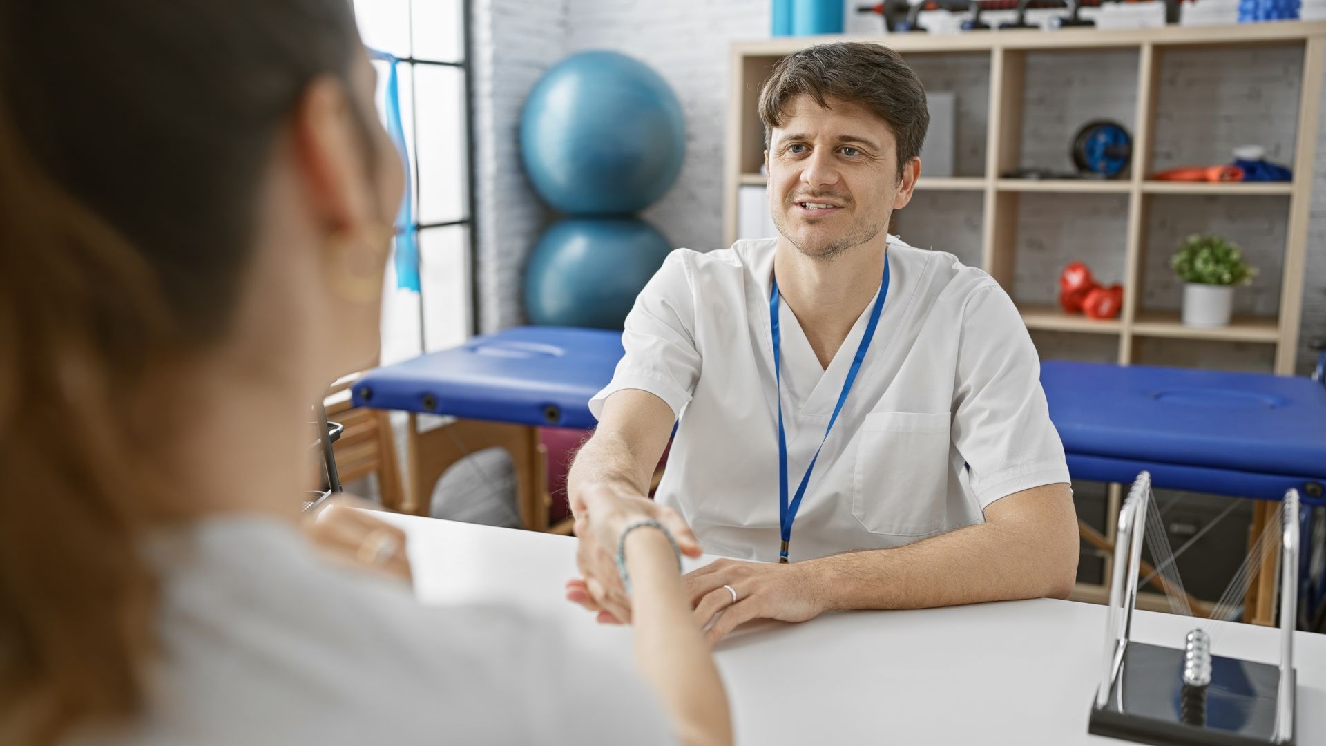 Physiotherapist shakes patient's hand at a desk in a clinic, smiling.
