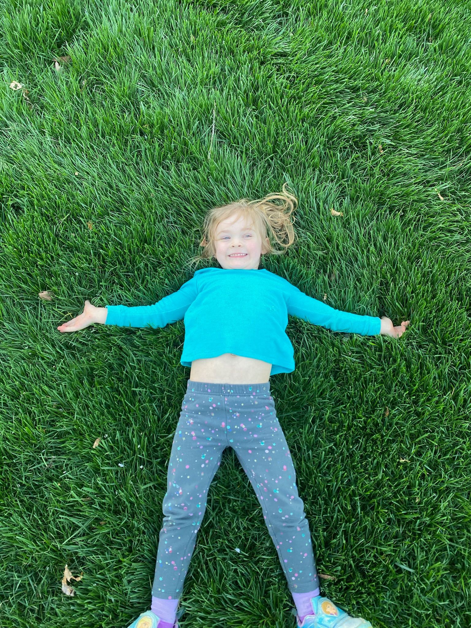 A little girl is laying on the grass with her arms outstretched.