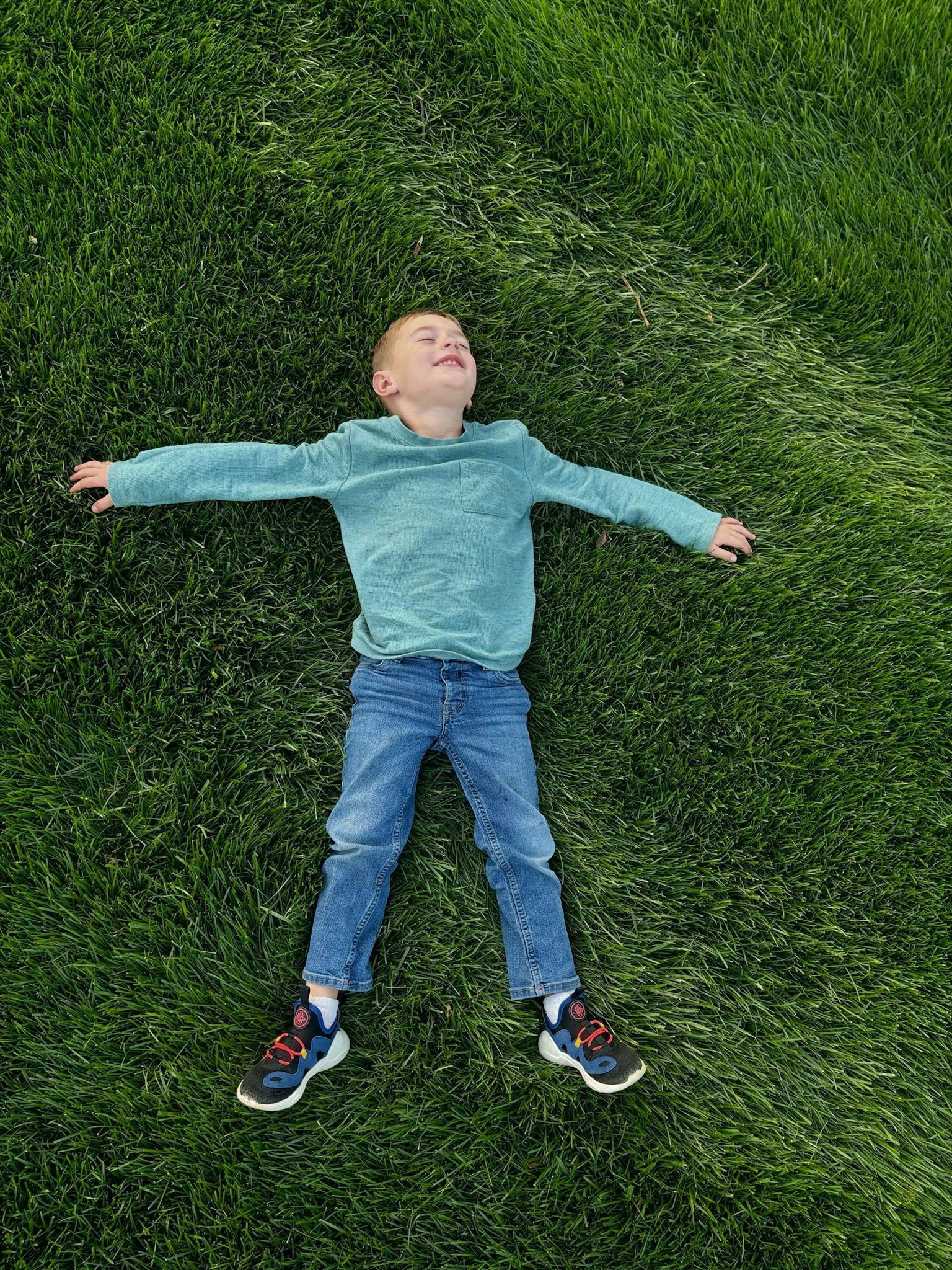 A young boy is laying on the grass with his arms outstretched.