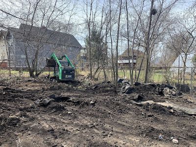 A green bobcat is digging in a dirt field in front of a house.