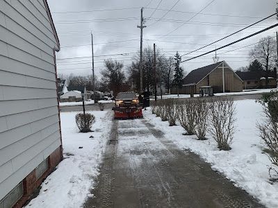 A snow plow is clearing snow from a driveway next to a house.