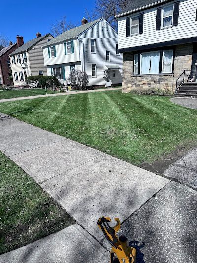 A lawn mower is sitting on the sidewalk next to a lush green lawn.