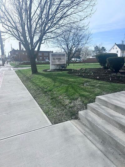A sidewalk with stairs leading up to a park with trees and bushes.