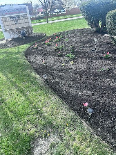 A garden with flowers and mulch in a park with a sign in the background.