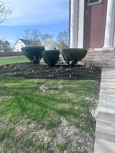 A brick house with a lush green lawn and bushes in front of it.