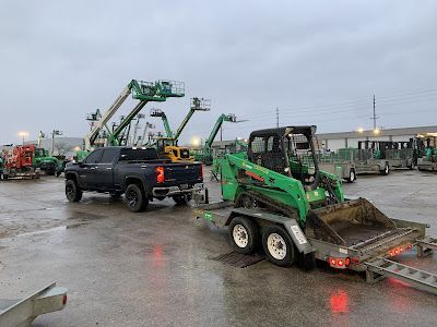 A truck is towing a green tractor on a trailer in a parking lot.