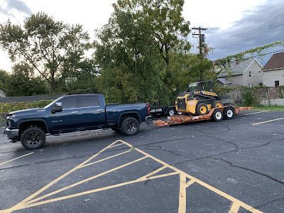 A blue truck is towing a yellow tractor in a parking lot.