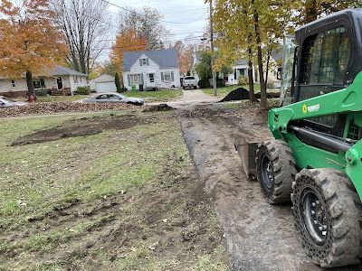 A green tractor is driving down a dirt road next to a house.