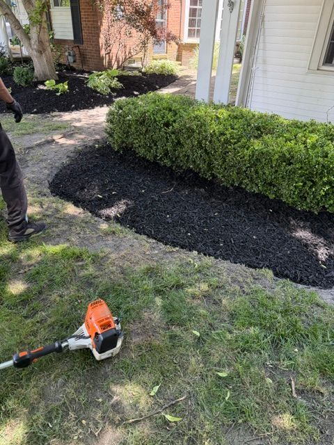 Orange trimmer on grass beside a mulched shrub bed and house exterior