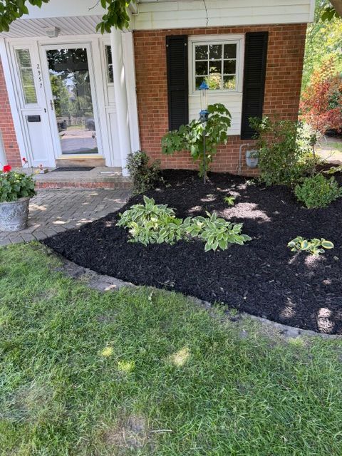 Front yard garden with mulch beds, green plants, brick house, and front door entrance