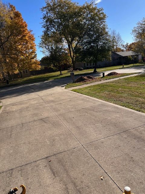 Concrete driveway leading into a residential neighborhood with fall foliage and clear blue sky.