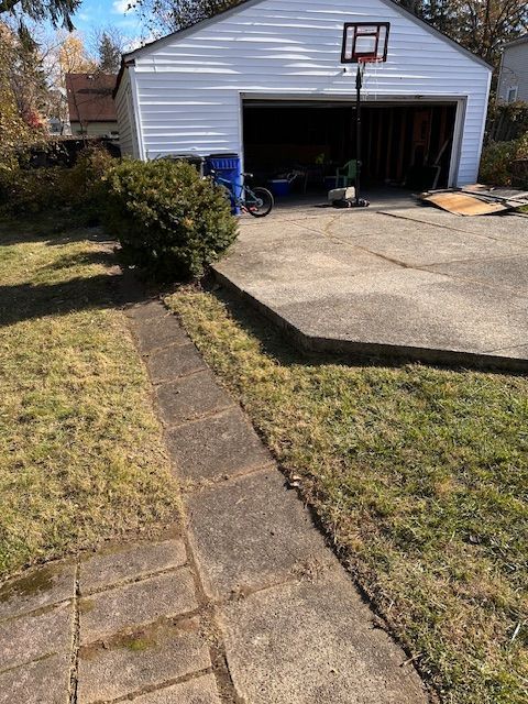 Concrete driveway and path leading to a white garage, grassy lawn, basketball hoop.