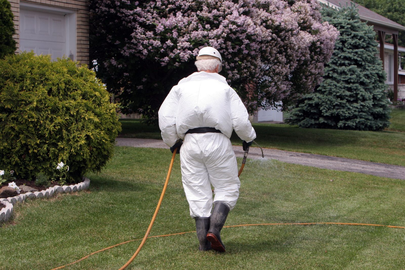 A man in a white suit is spraying a lawn with a hose.