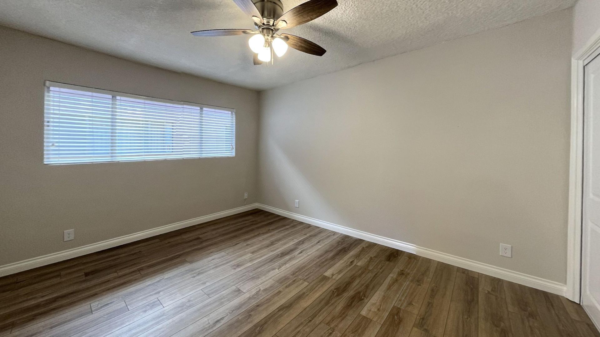 Empty bedroom with wood-look flooring, a window with blinds, and a ceiling fan.