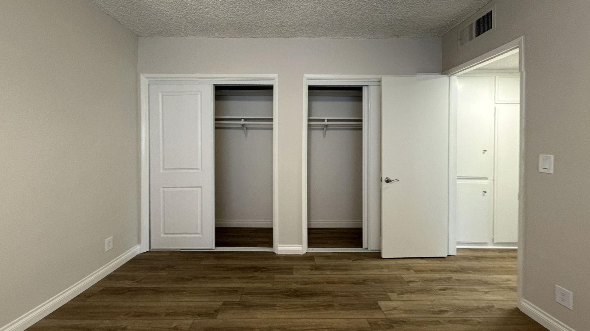 Empty bedroom with brown flooring, two closets, and a partially open door.