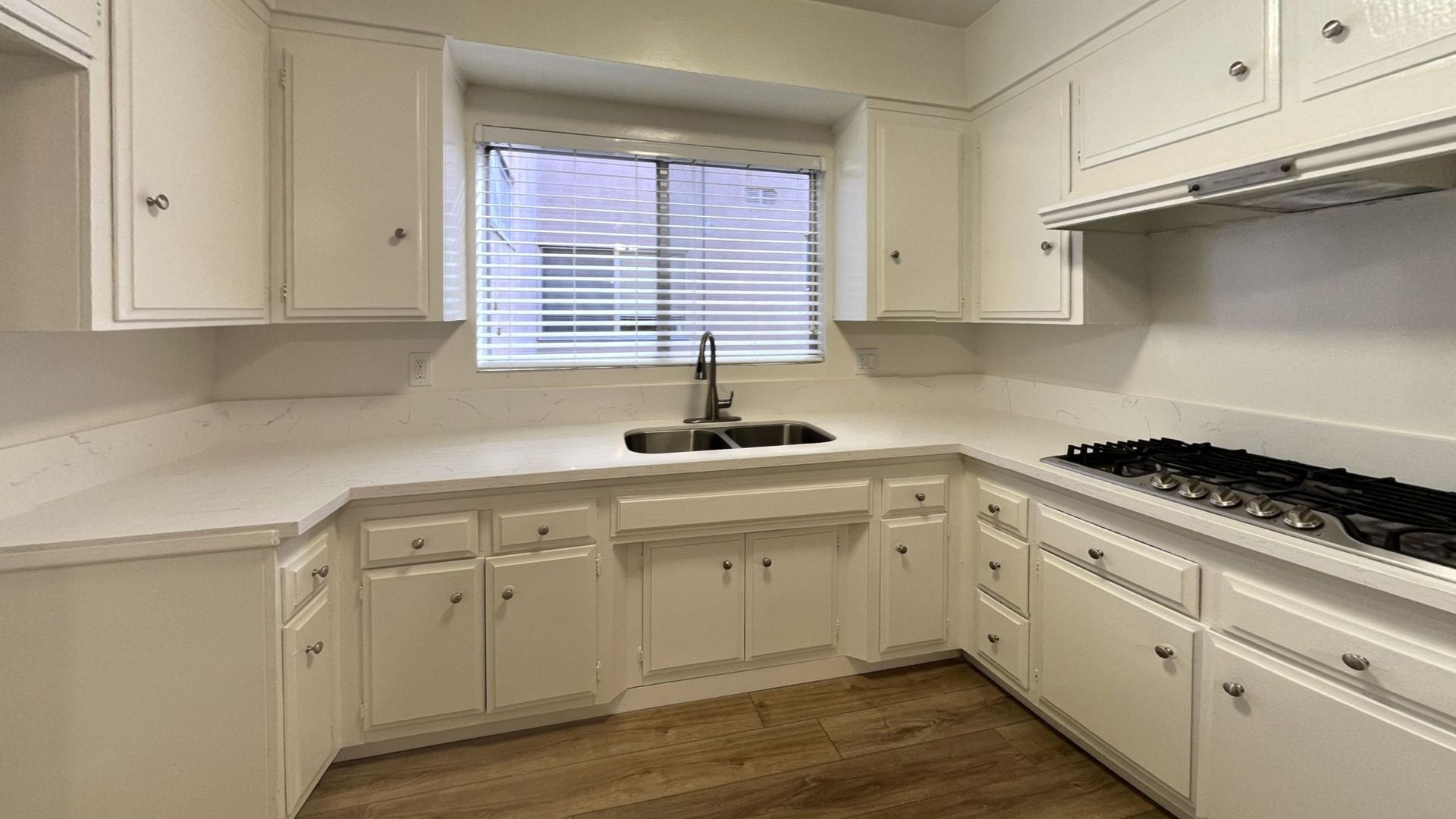 White kitchen with cabinets, countertops, and a gas range. A window sits above a sink.