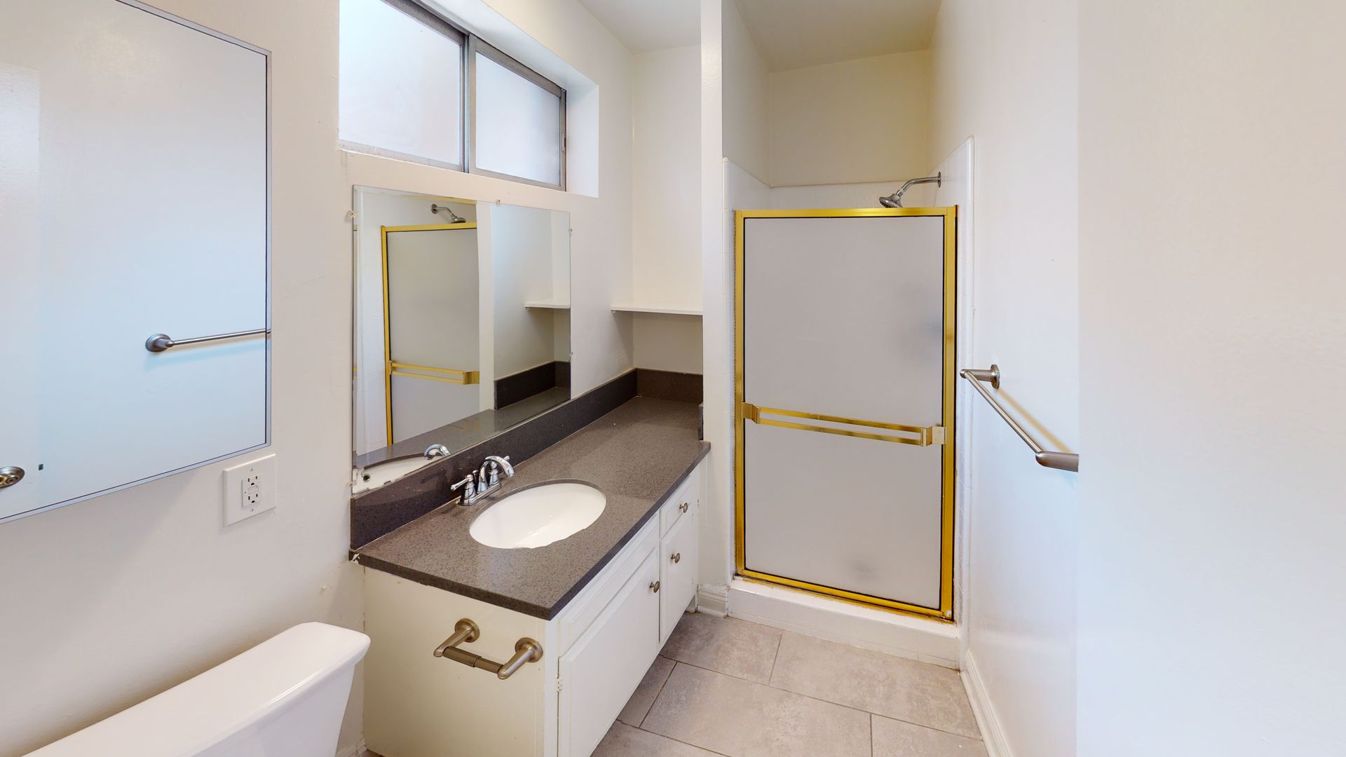 Bathroom with white walls, vanity, shower stall, toilet, and a window.