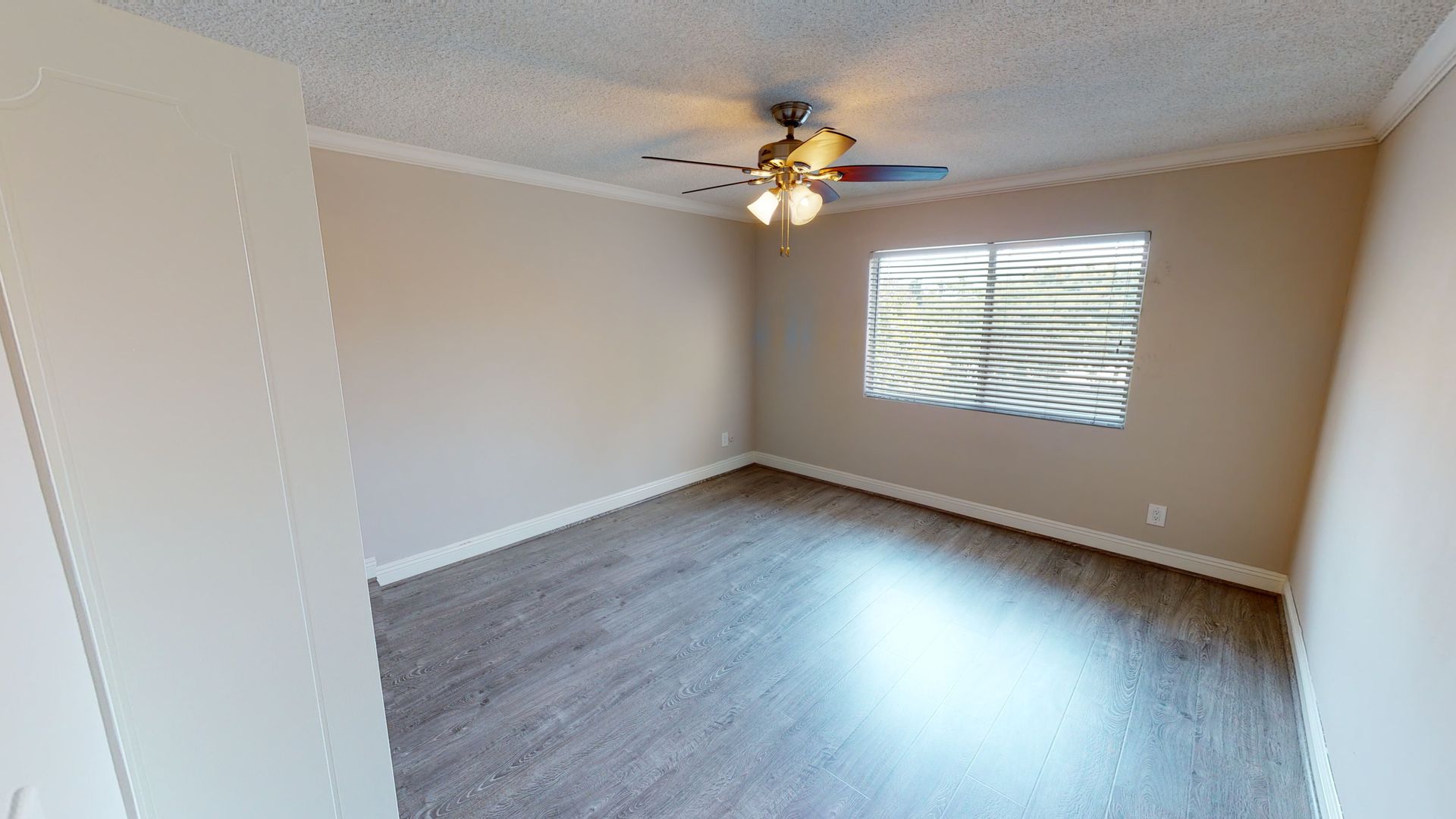 Empty room with gray flooring, a window, ceiling fan, and beige walls.