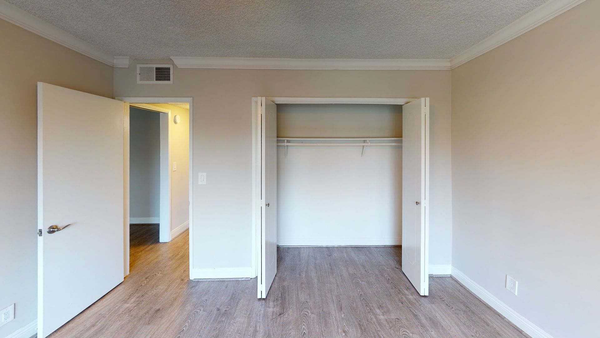 Empty room with closet and open doorway, wood-look flooring, beige walls.