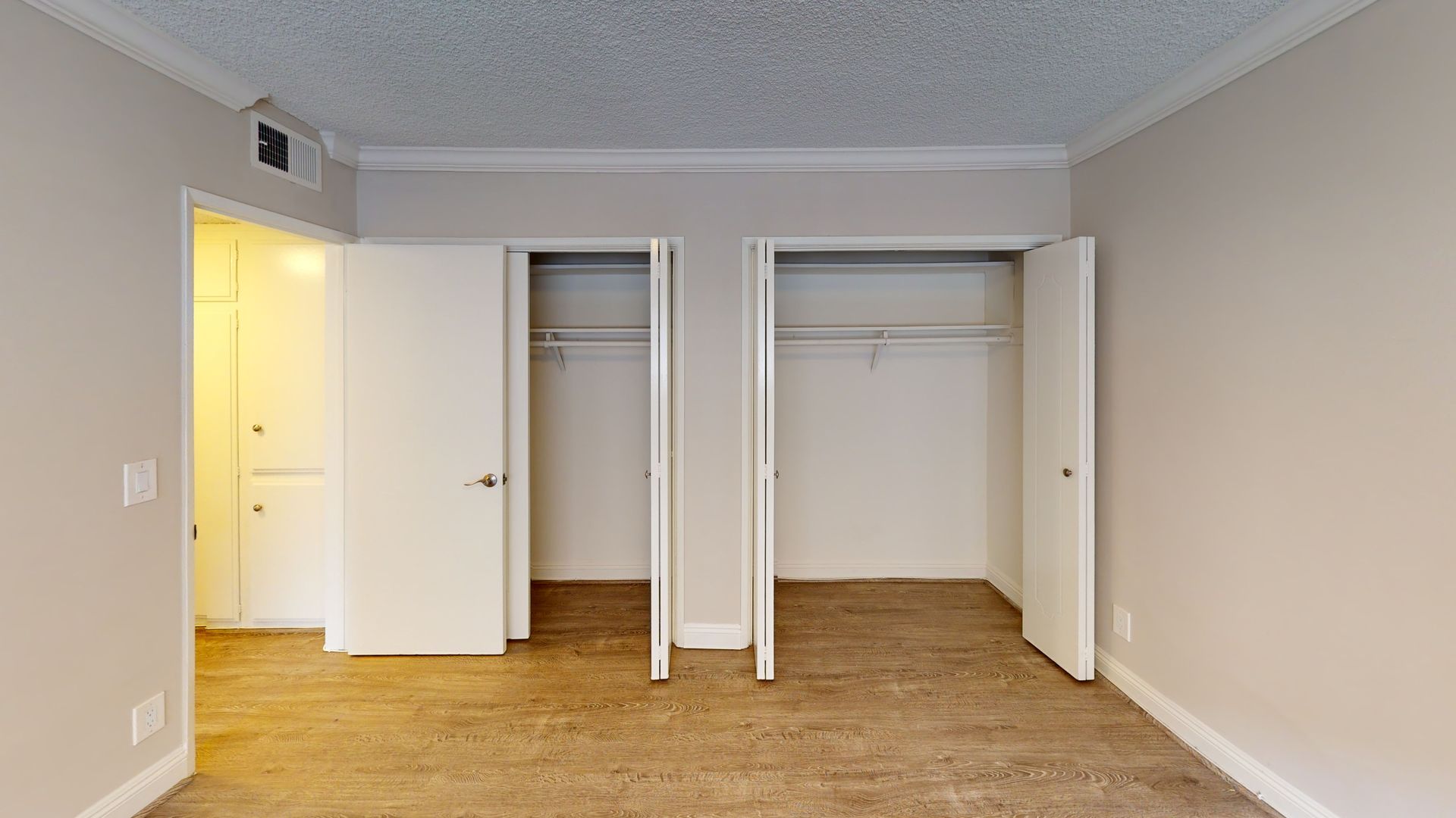 Empty bedroom with two closets and a doorway, beige walls, carpet, and white ceiling.
