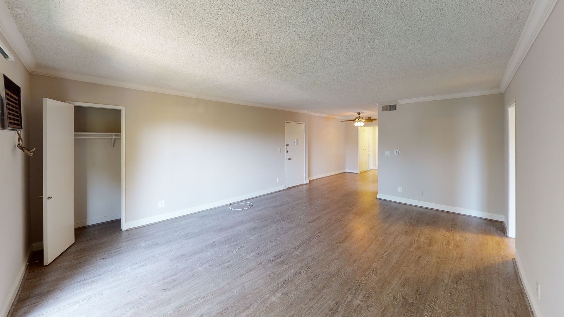 Empty apartment interior with neutral-colored walls and dark wood-look flooring. Closet and doorway visible.