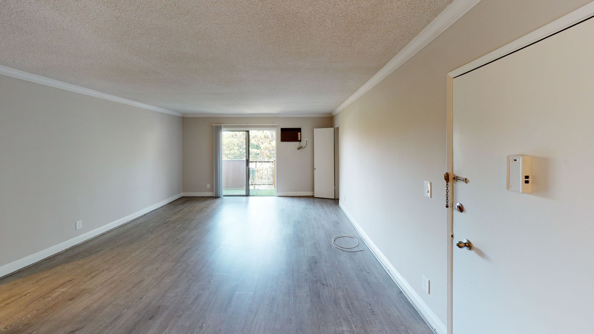 Empty living room with wood-look flooring, balcony doors, and a white door with hardware.