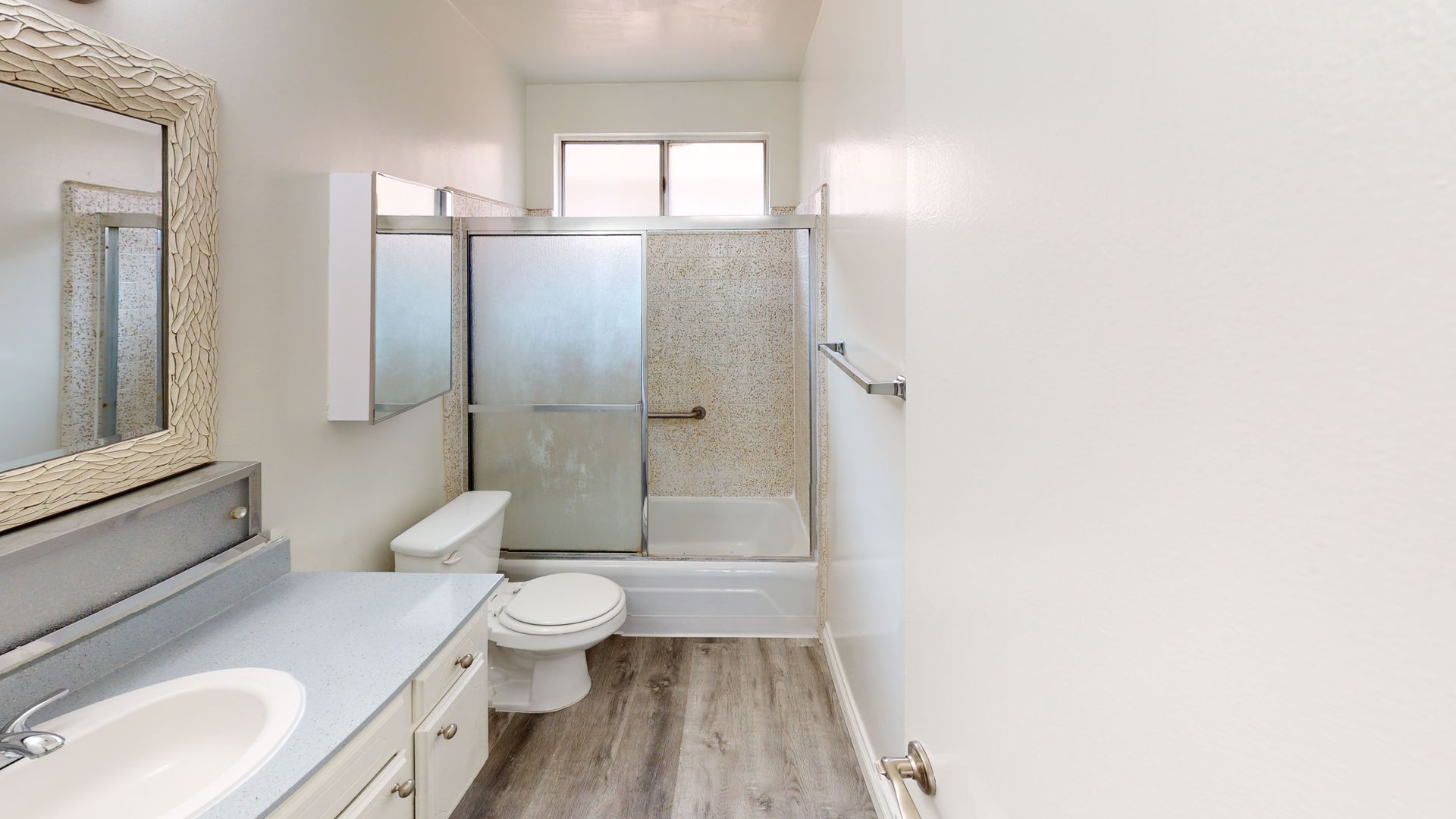 Bathroom with a sink, toilet, shower, and window. Light gray cabinets and flooring.