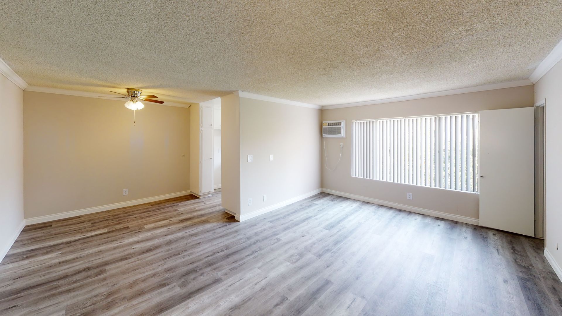 Empty living room with gray wood-look flooring, white walls, and a window with blinds.