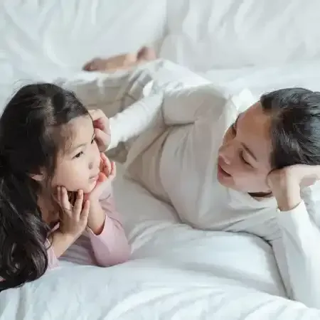 Woman and child lying on a bed, looking at each other, engaging in a conversation.
