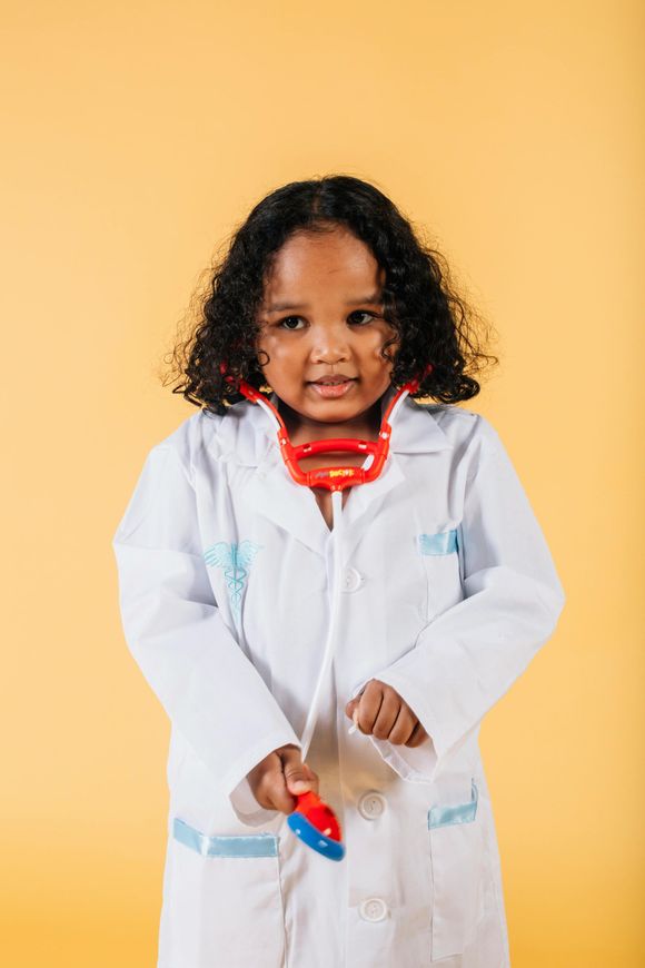 Girl wearing a doctor's coat and stethoscope, looking curious, on a yellow background.